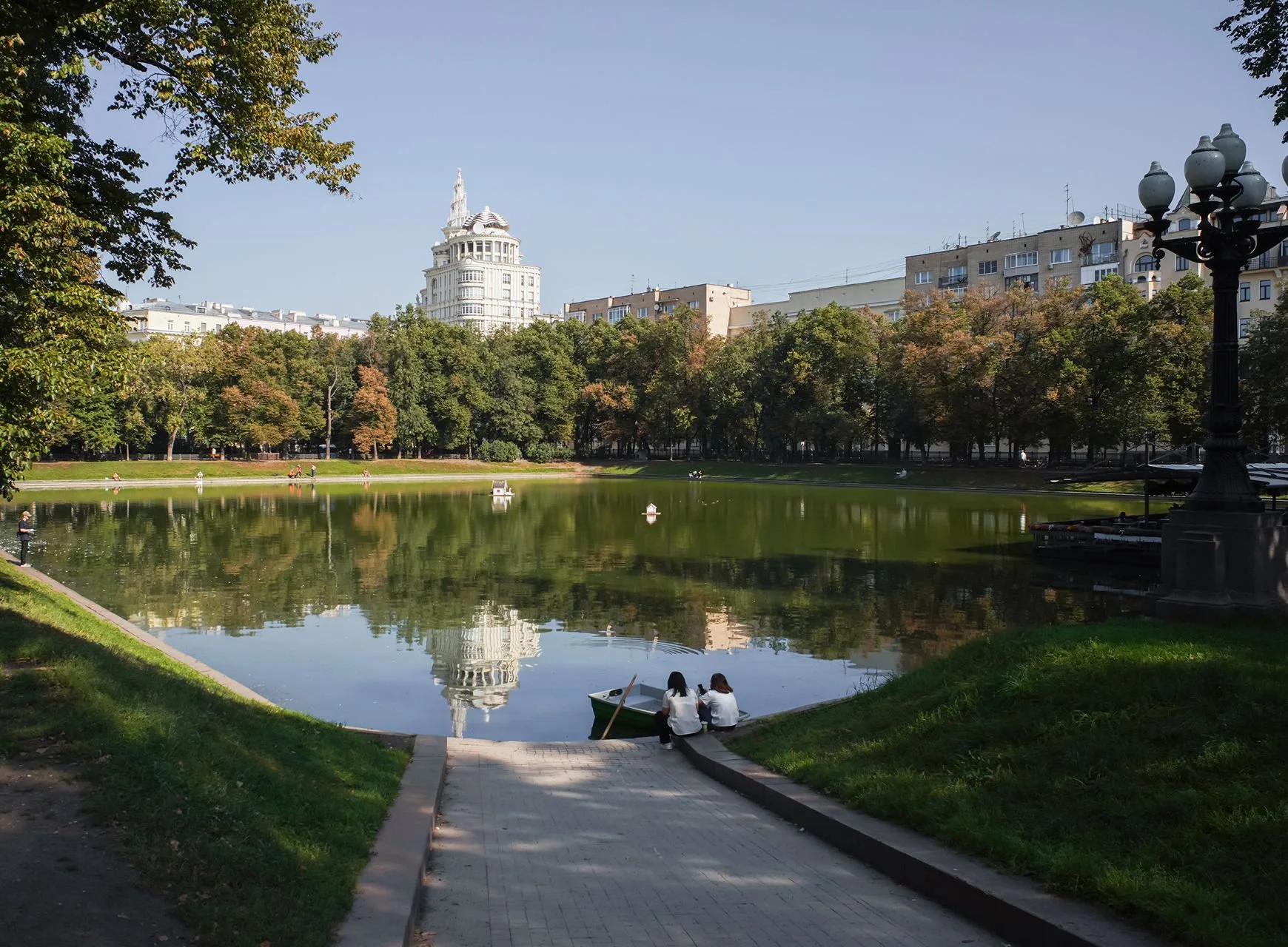 Патриарший пруд: вода, деревья вдоль набережной, люди на дорожке