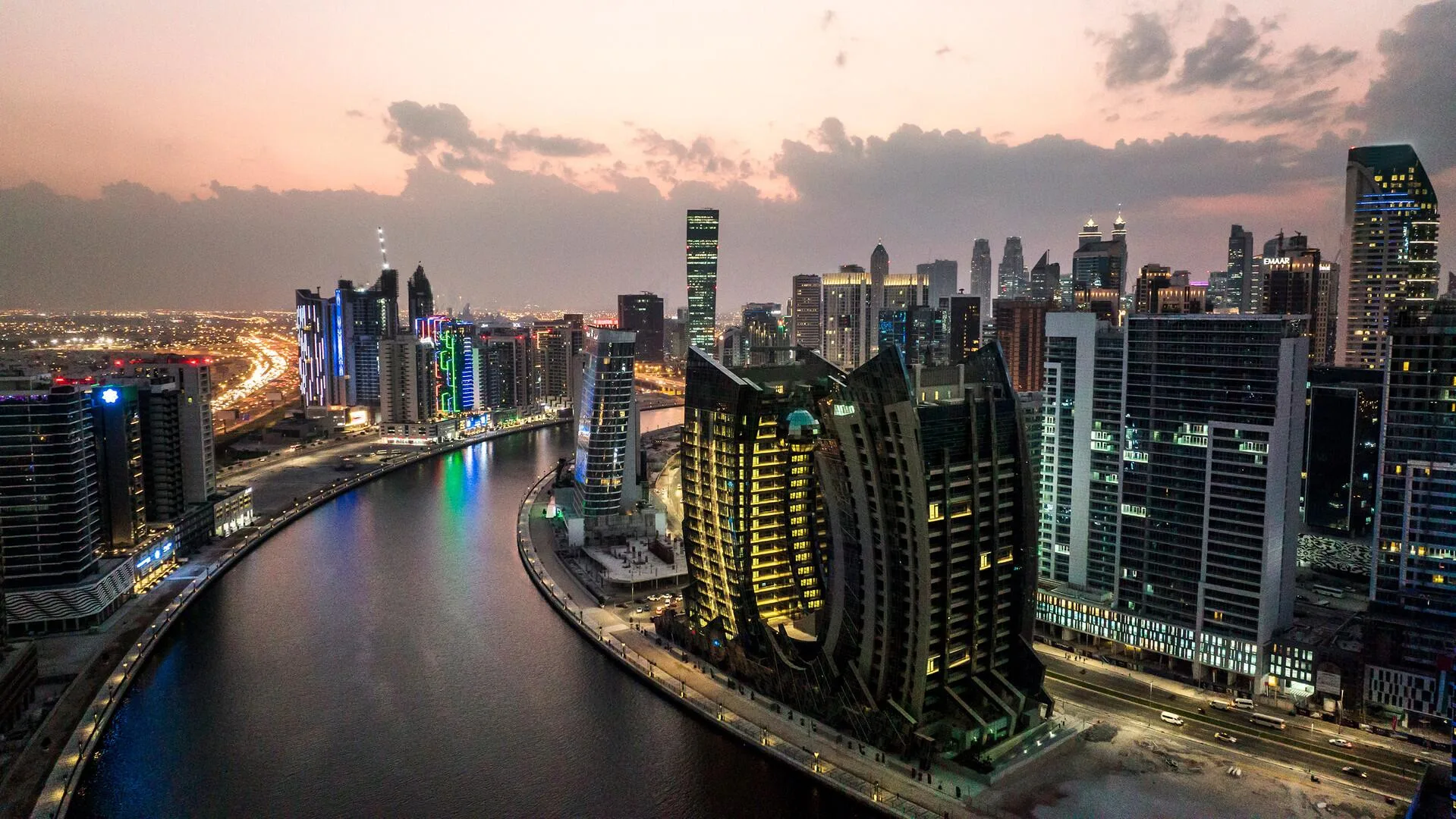 Изгиб Дубайского канала и башня в сумерках на фоне Downtown Dubai
