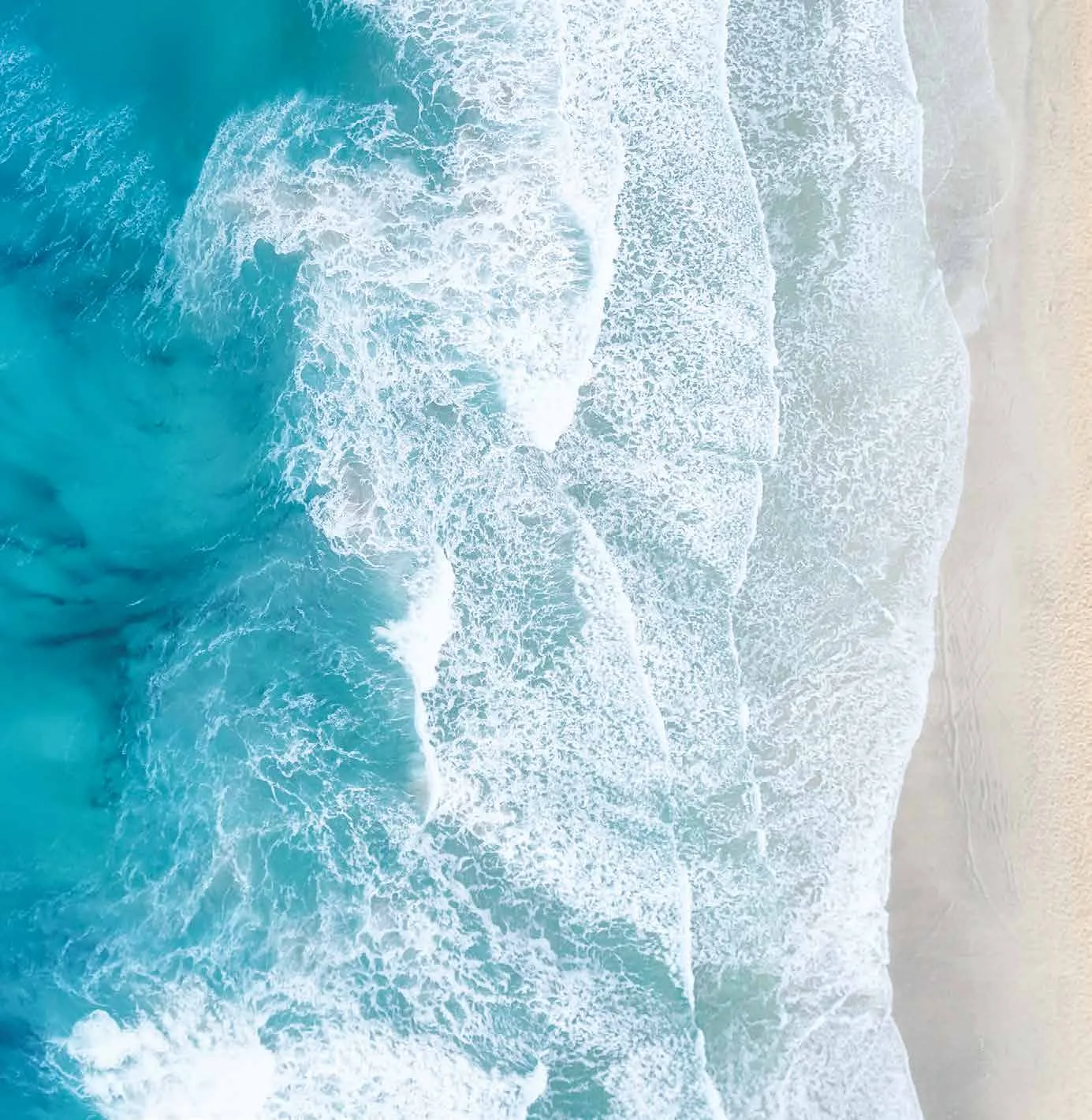 Turquoise waves washing over a sandy shore, seen from above