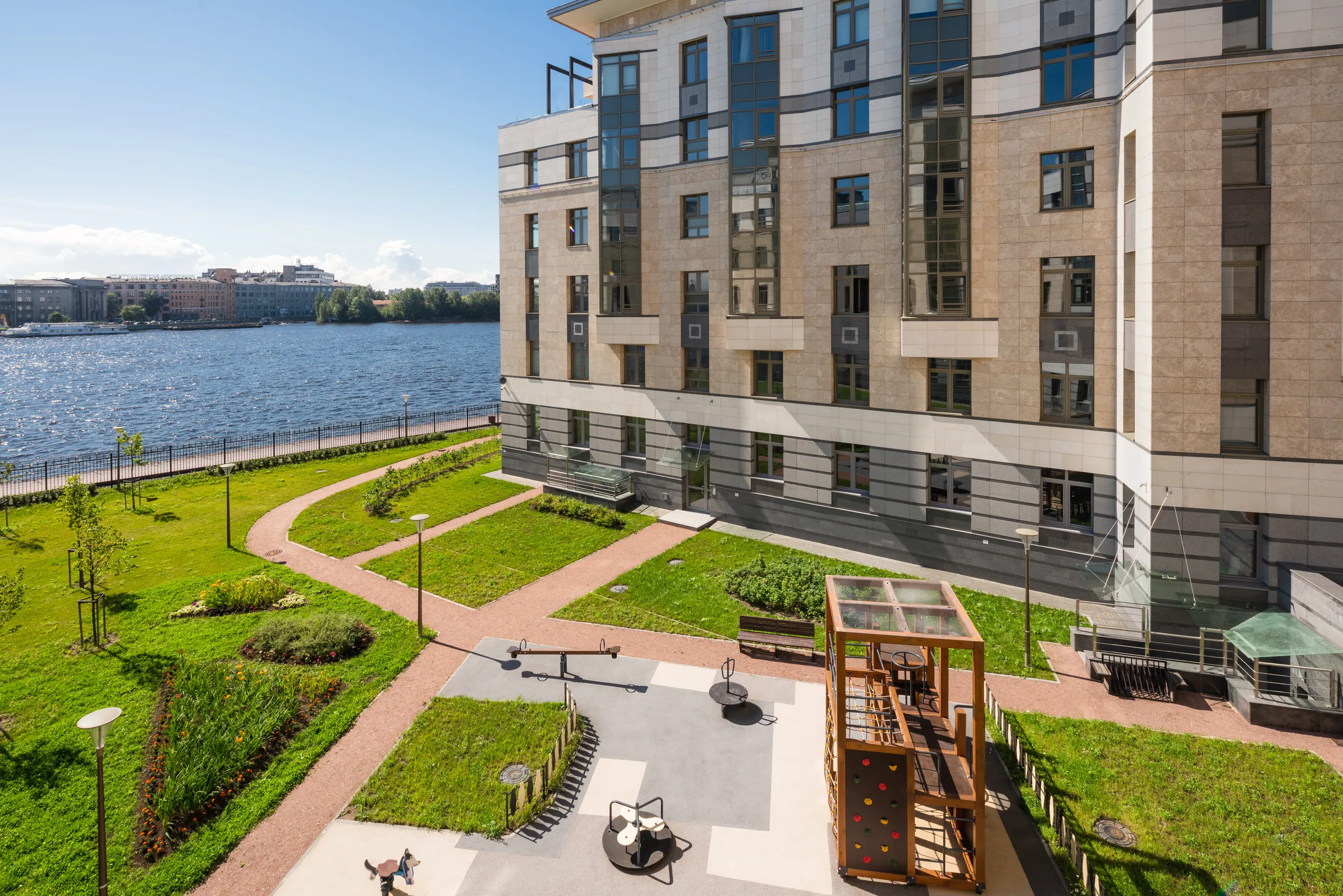 Двор Royal Park днём: газоны, дорожки, детская площадка, каменный фасад корпуса, за деревьями река