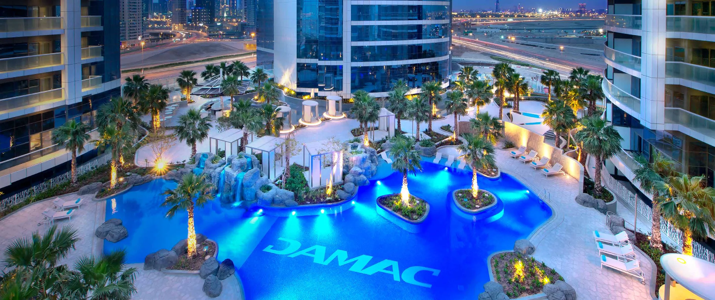 Бассейн на подиуме DAMAC Towers вечером, пальмы и шезлонги